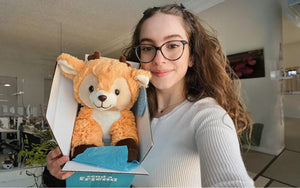 An image of a girl smiling while holding up a Someone Loves You box with Daphne the Deer inside 