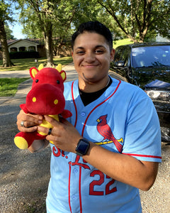 Photo of person standing outdoors smiling while holding red and yellow Duke the Dragon plushie