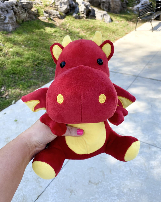 Photo of hand holding red and yellow Duke the Dragon plushie outdoors 
