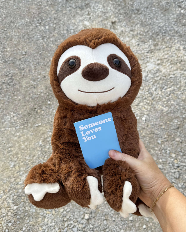 Photo of hand holding a note card with 14 inch Jumbo Sam the Sloth with concrete in the background