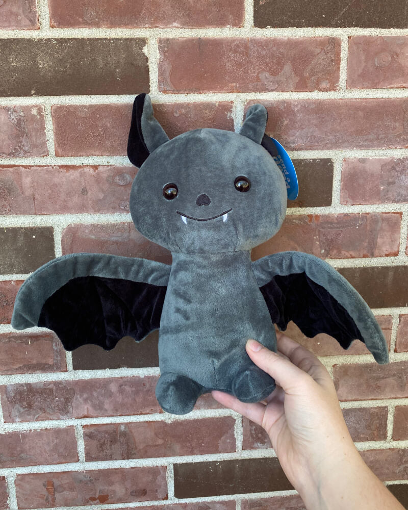 Photo of a hand holding black Binks the Bat plushie up against a brick wall
