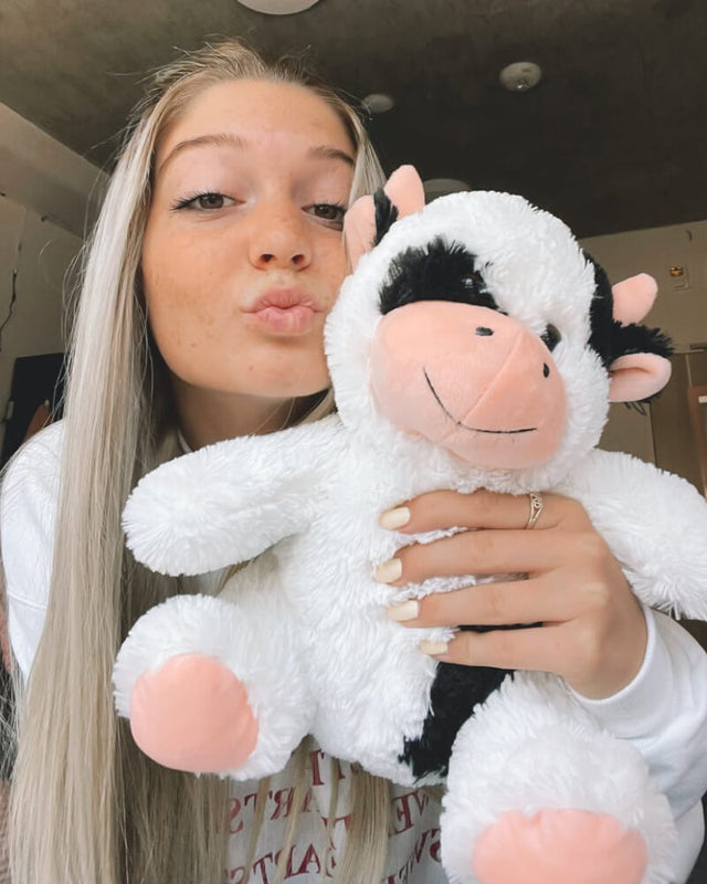 Photo of person making kissing face while holding white and black Cooper the Cow plushie
