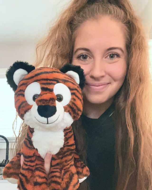 Photo of person grinning while holding orange and black striped Tilly the Tiger plushie near face