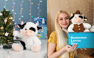 cow stuffed animal decorating Christmas tree next to woman holding cowboy cow in blue "someone loves you" box