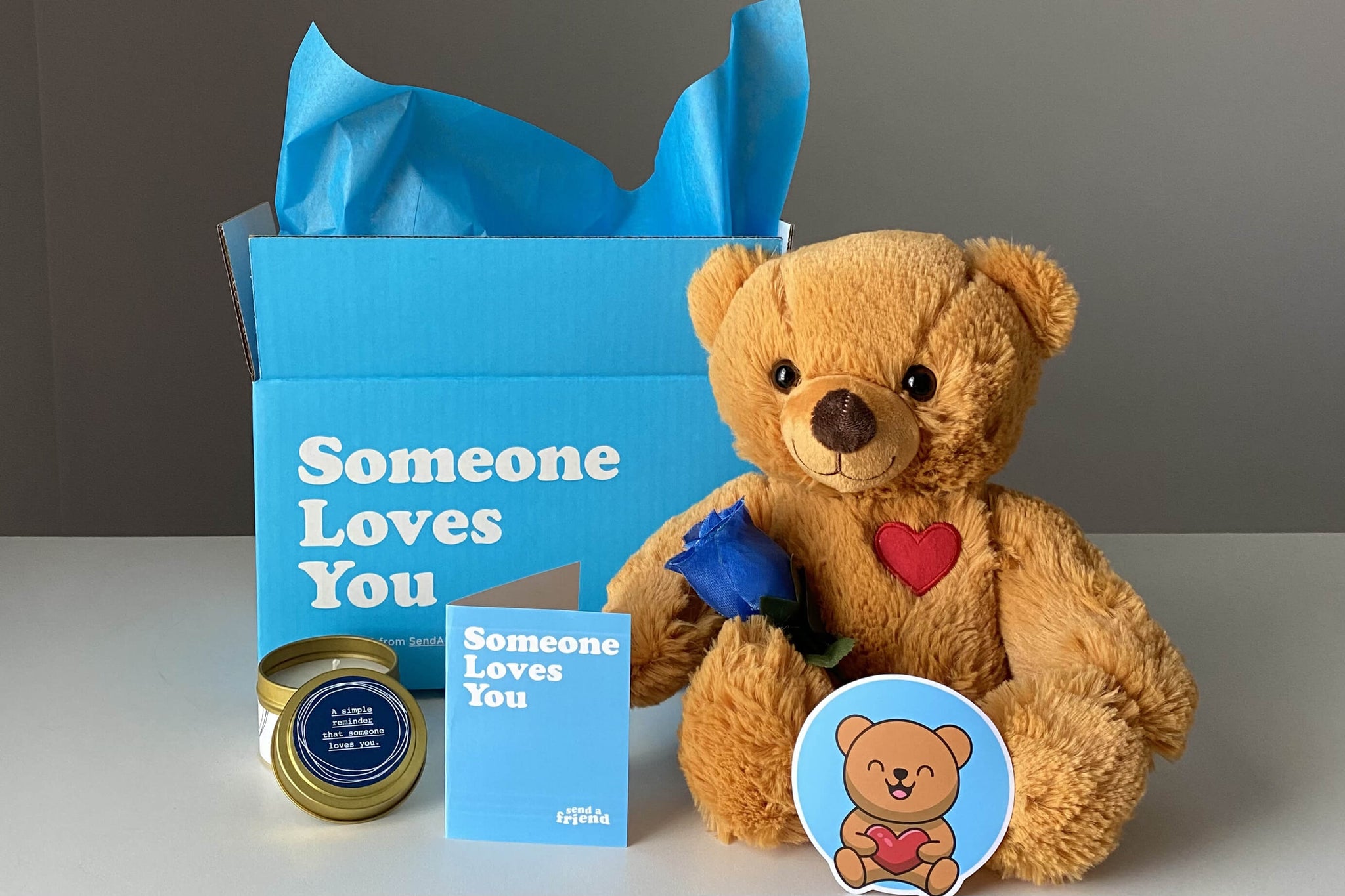tan teddy bear with sticker, candle, and notecard next to box