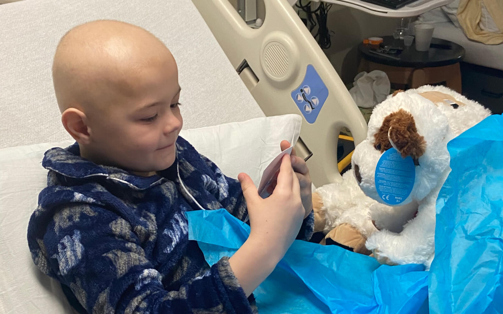 child in hospital bed receiving a stuffed animal care package