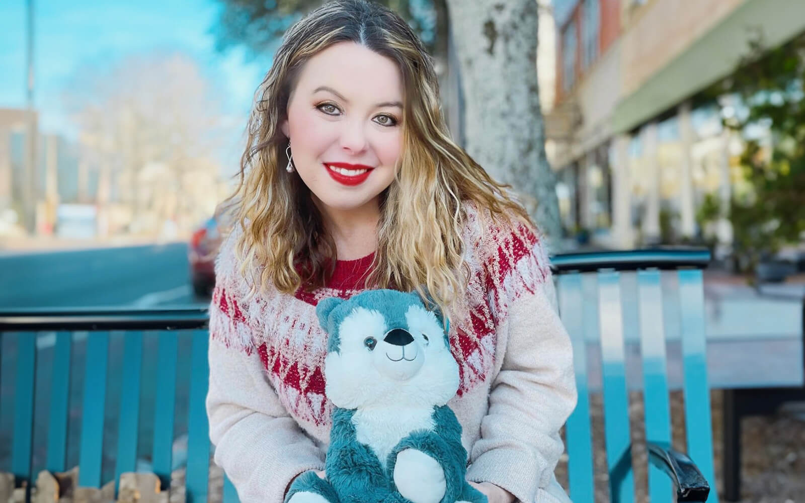 An image of a woman sitting on a blue bench holding Winston the Wolf