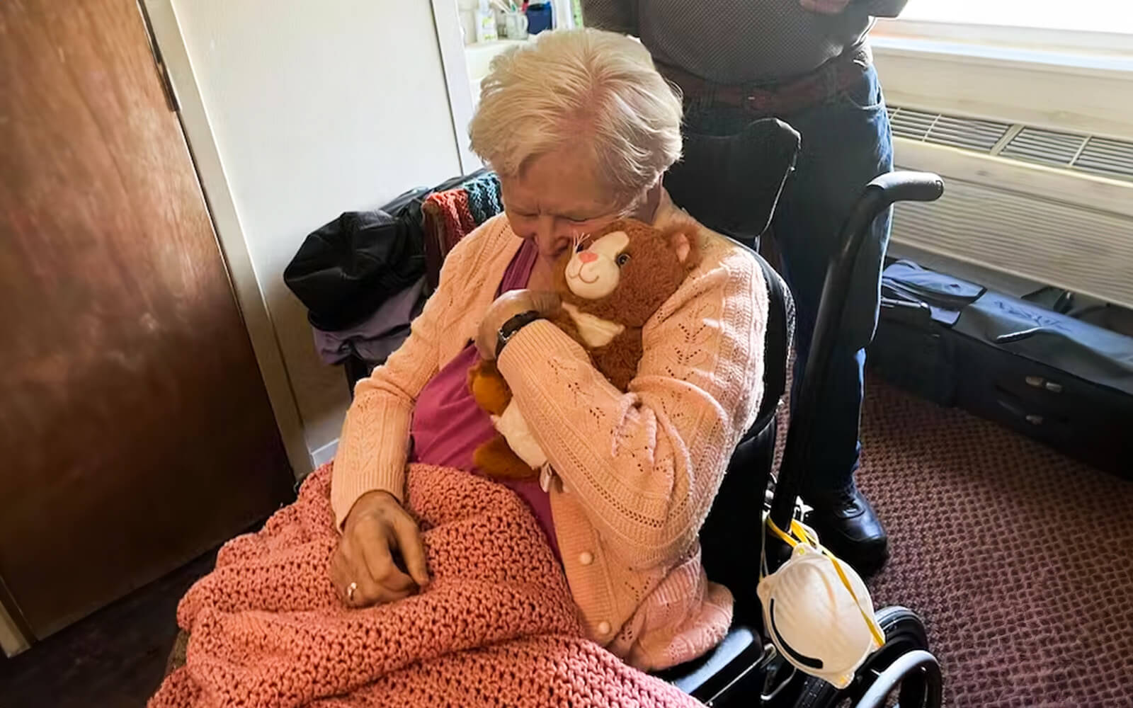 An older woman sitting in a wheelchair hugging Kiwi the Kitten