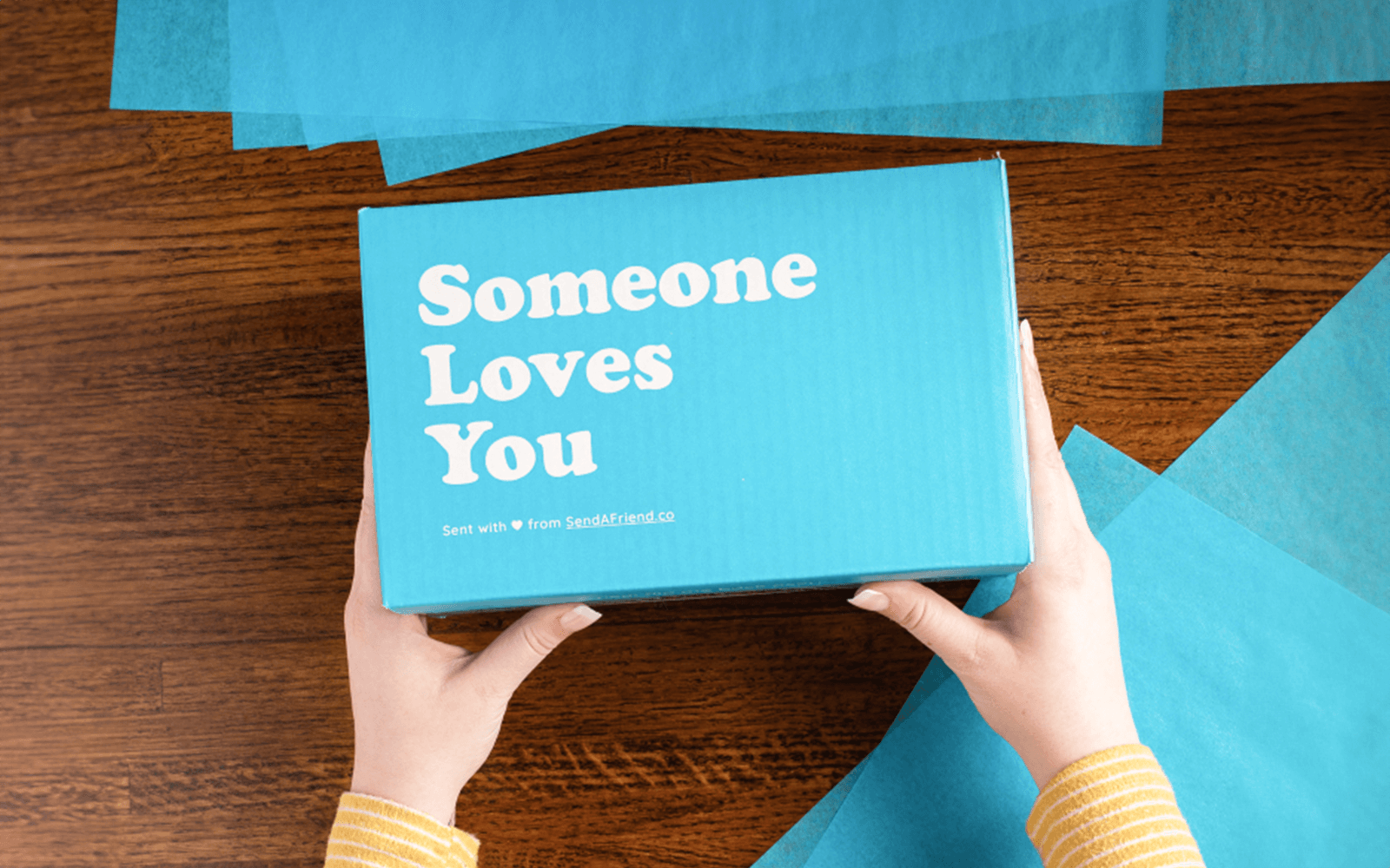 Photo of hands holding Someone Loves You box surrounded by blue tissue paper