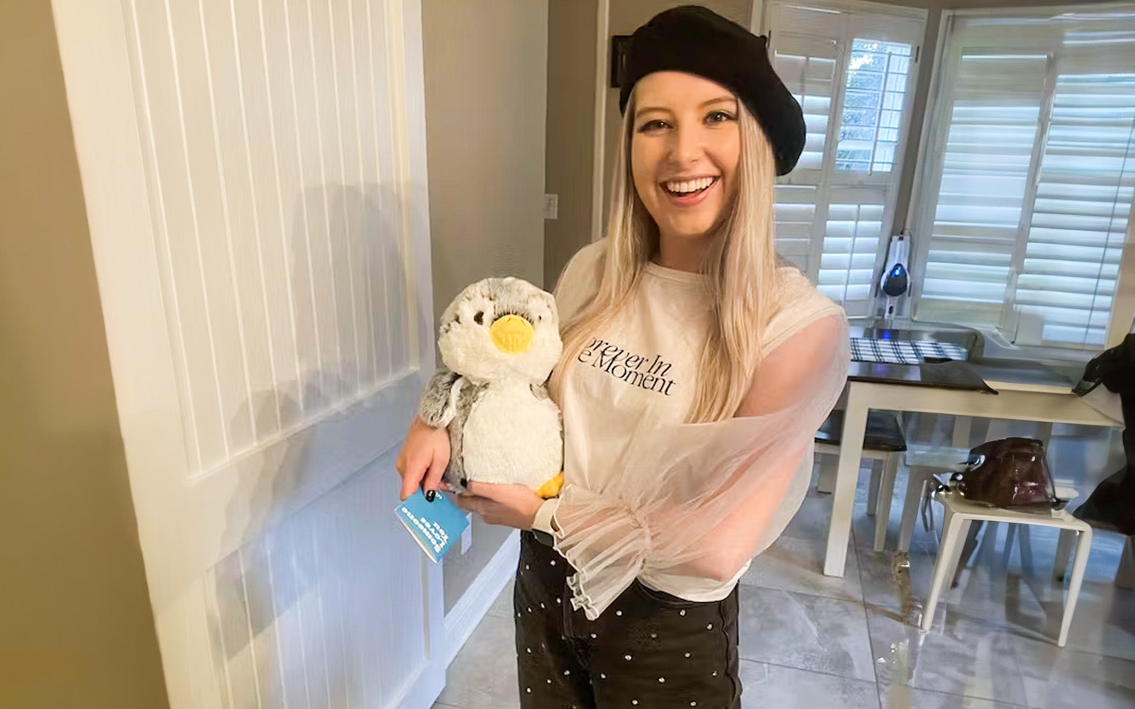 An image of a girl smiling holding Pepper the Penguin and a note card
