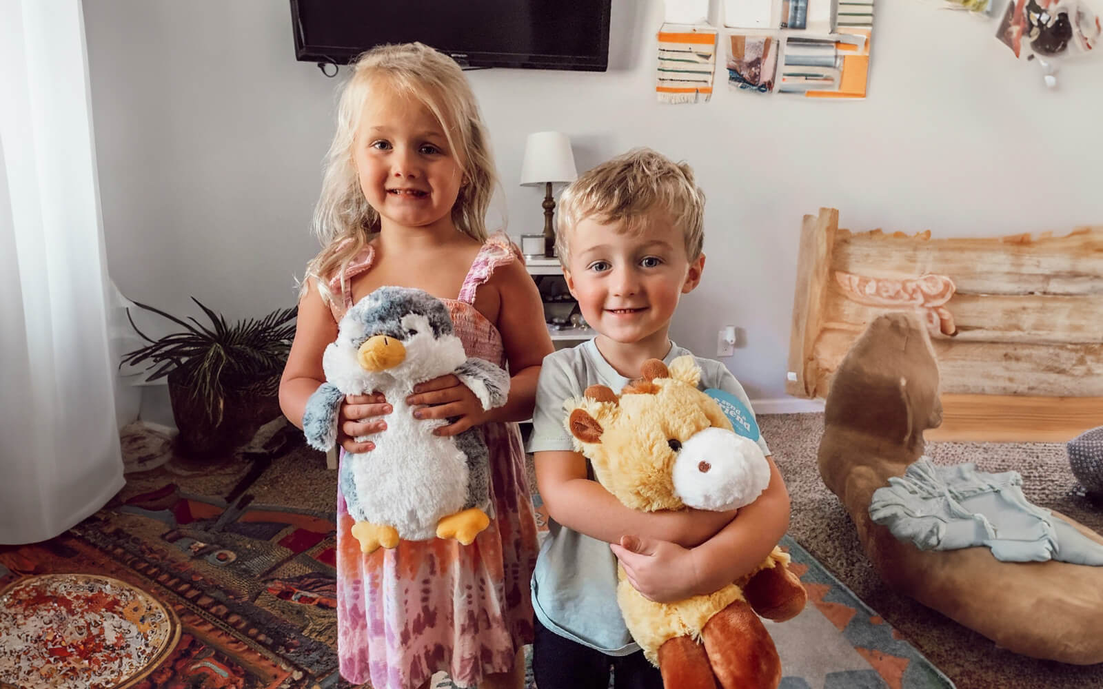 An image of two children smiling, one holding Pepper the Penguin and the other holding George the Giraffe