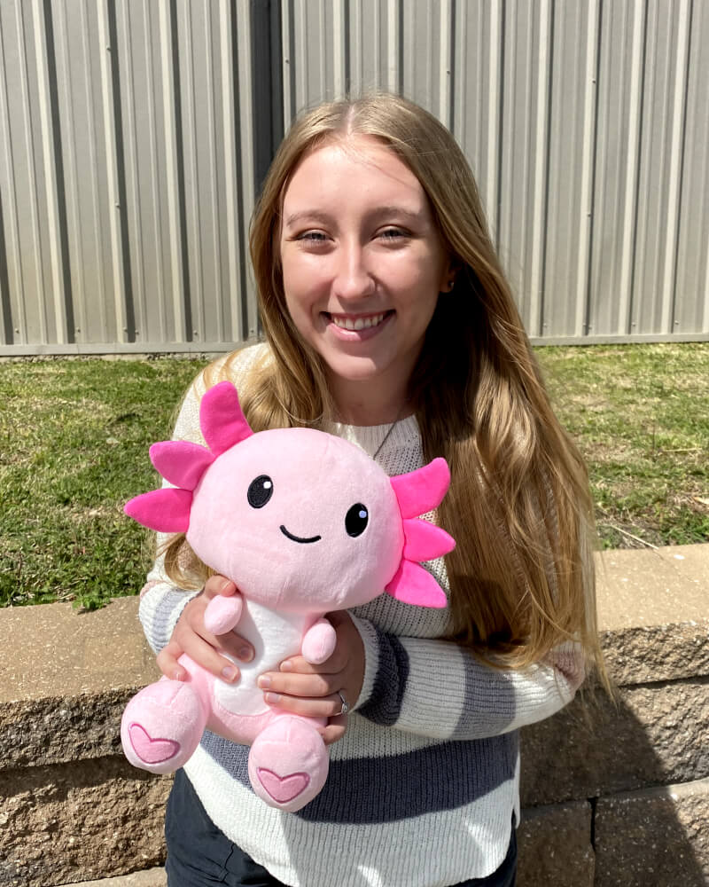 Photo of person standing outdoors holding pink axolotl plushie