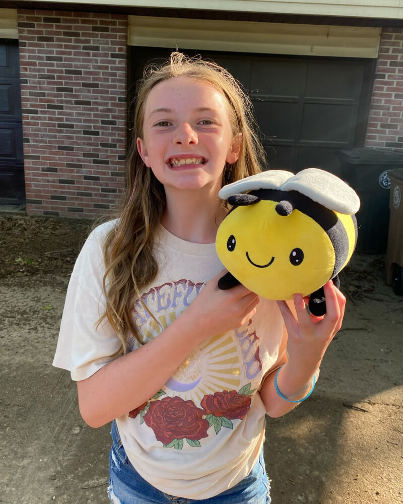 Photo of an adolescent standing outside holding yellow and black Beatrice the Bee