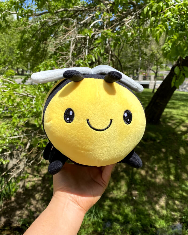 Photo of hand holding up yellow and black Beatrice the Bee outdoors