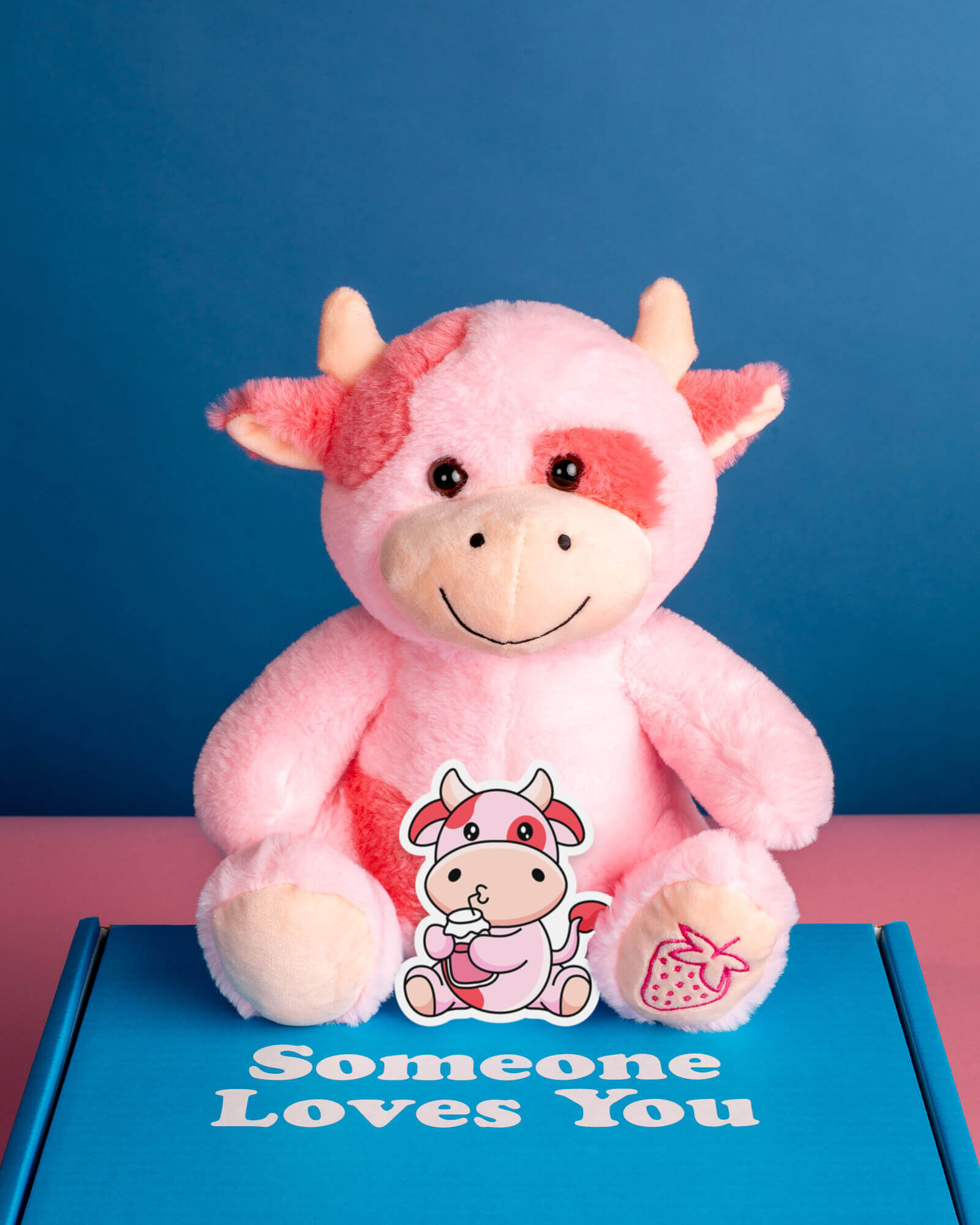 Photo of Sally the Strawberry Cow plushie sitting on Someone Loves You box with matching sticker