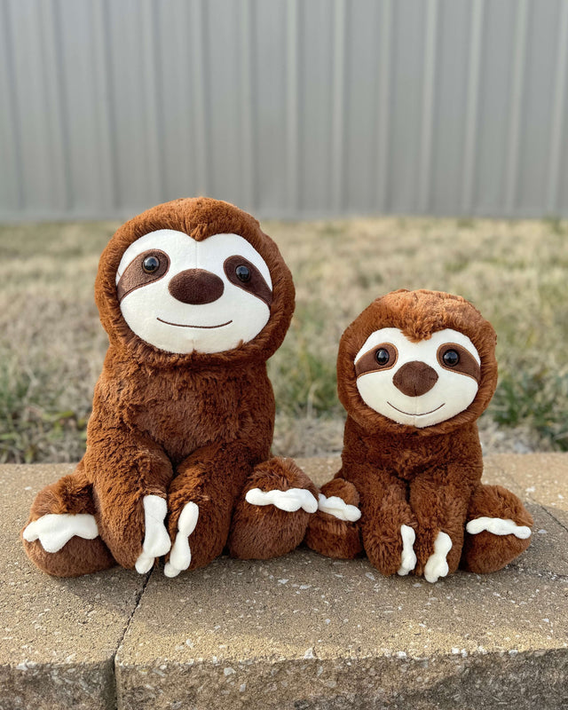 Photo of 10 inch and 14 inch brown Sam the Sloth plushies sitting on bricks with grass in the background
