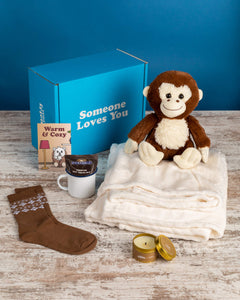 Photo of Maria the Monkey plushie with Cozy Bundle: promo card, hot cocoa, mug, socks, candle, cozy blanket