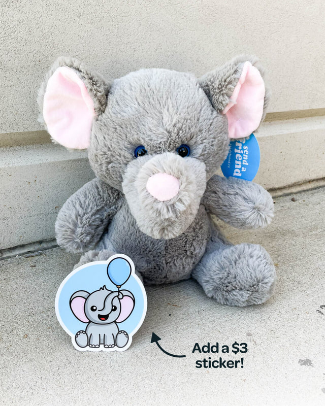 Photo of grey Eli the Elephant plushie sitting on concrete with matching sticker that is available to purchase for additional $3