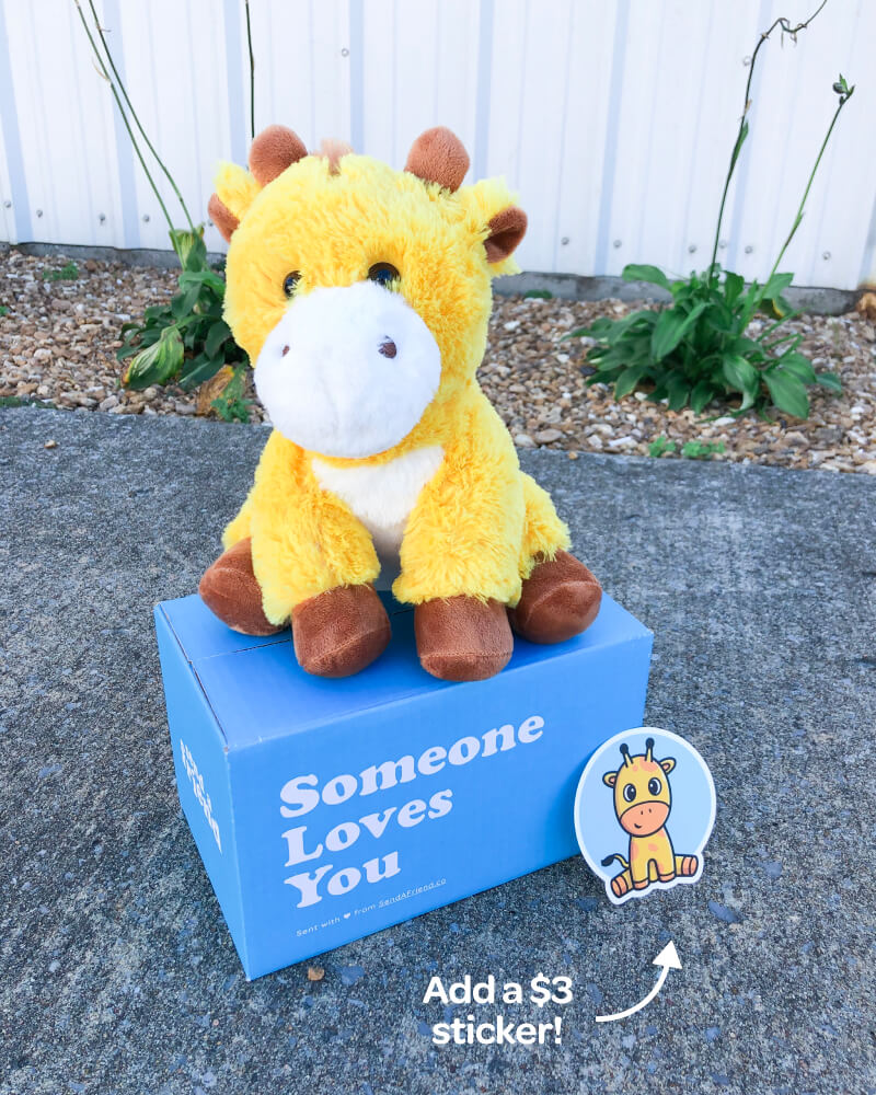 Photo of yellow George the Giraffe sitting outdoors on Someone Loves You box. Also pictured: Matching sticker which can be purchased for $3