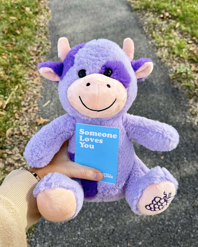 Photo of hand holding purple cow plushie with notecard