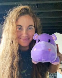 Photo of person smiling while holding purple Harper the Hippo plushie near face
