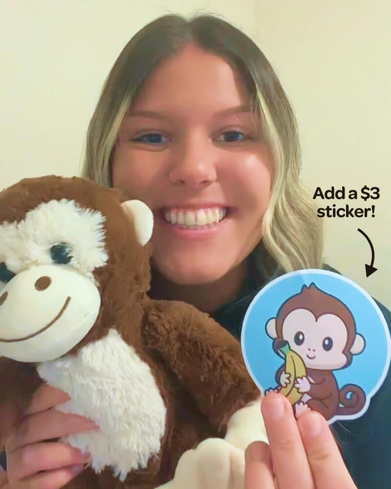 Photo of person smiling while holding Maria the Monkey plushie and matching sticker which is available to purchase for an additional $3