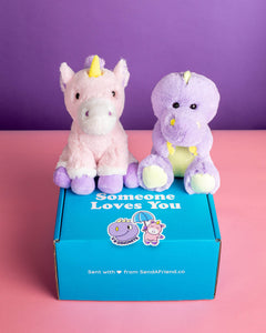 Photo of Unique the Unicorn and Dexter the Dino plushies sitting on Someone Loves You box with matching stickers. 