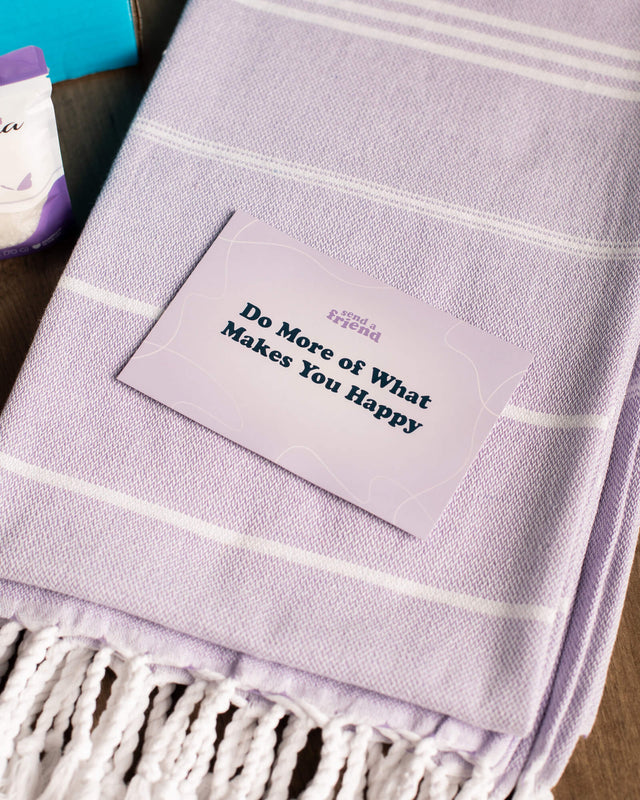 Photo of promotional card sitting on top of Lavender colored Turkish towel included in Deluxe Self Care Bundle