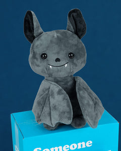 Photo of Binks the Bat plushie sitting on blue box in front of a blue background