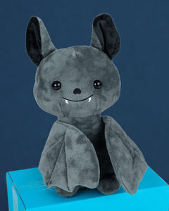 Photo of Binks the Bat plushie sitting on a blue box in front of a blue background