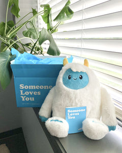 Photo of white Yuka the Yeti with blue face and yellow horns sitting in a window sill with open Someone Loves You box and note card