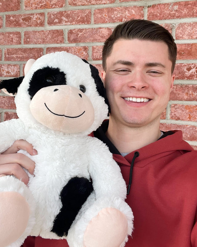 Photo of person smiling while holding Jumbo Cooper the Cow 14 inch black and white plushie close to face
