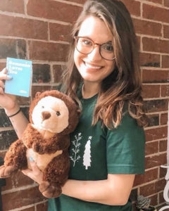 Photo of person smiling while holding brown Oliver the Otter plushie and note card