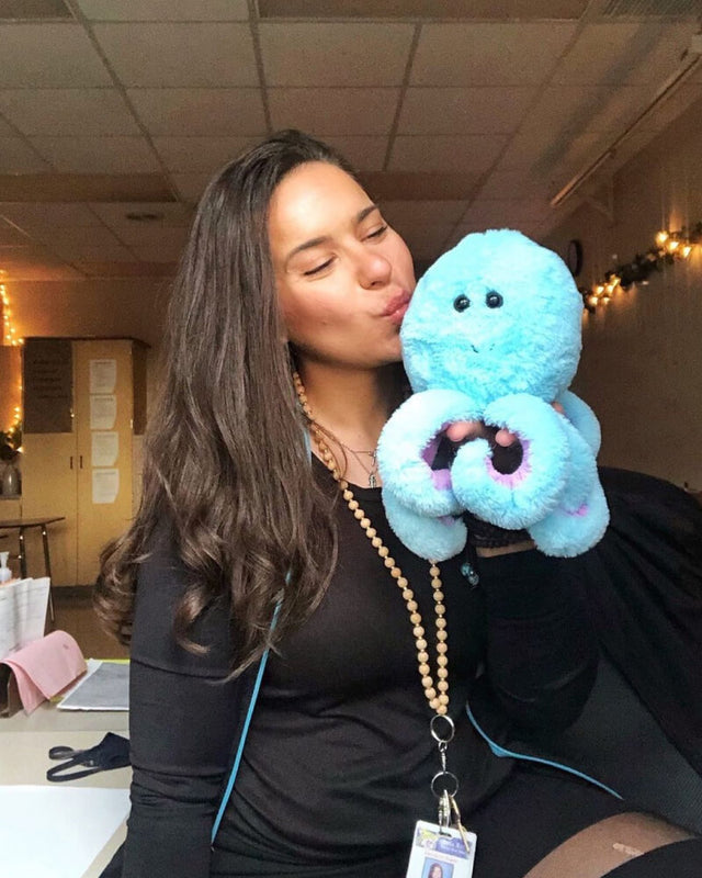 Photo of person holding blue Ollie the Octopus near face with puckered lips as if to kiss the plushie