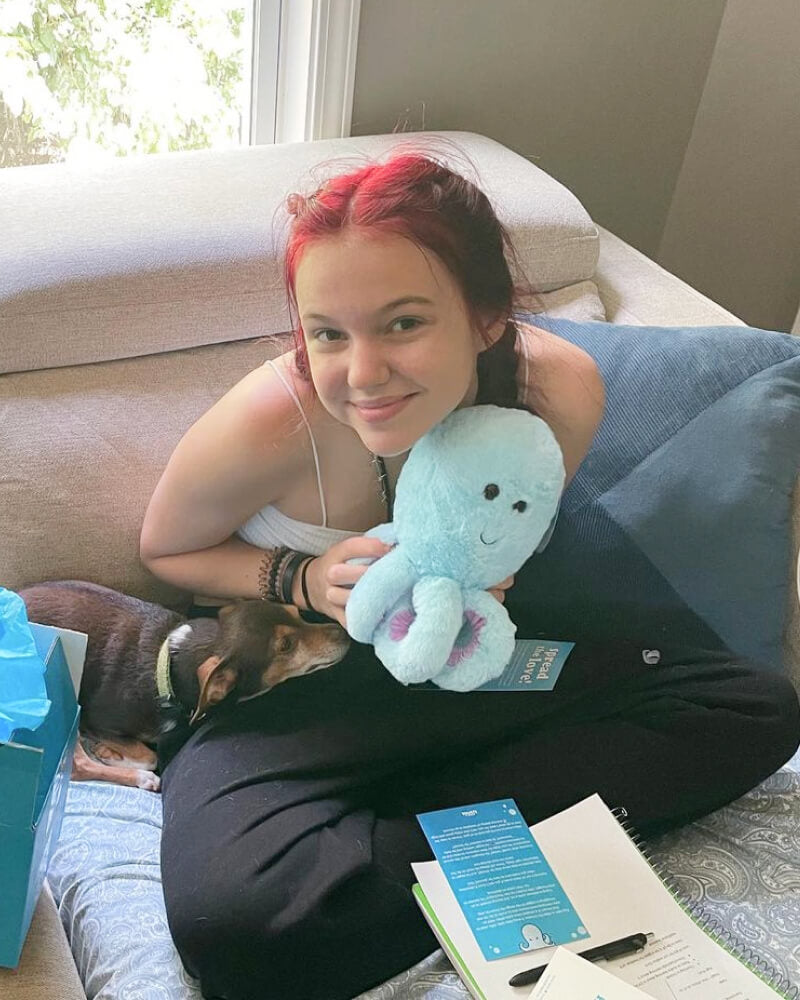 Photo of person smiling while holding blue Ollie the Octopus plushie 