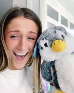 Photo of person smiling holding grey and white Pepper the Penguin plushie near face