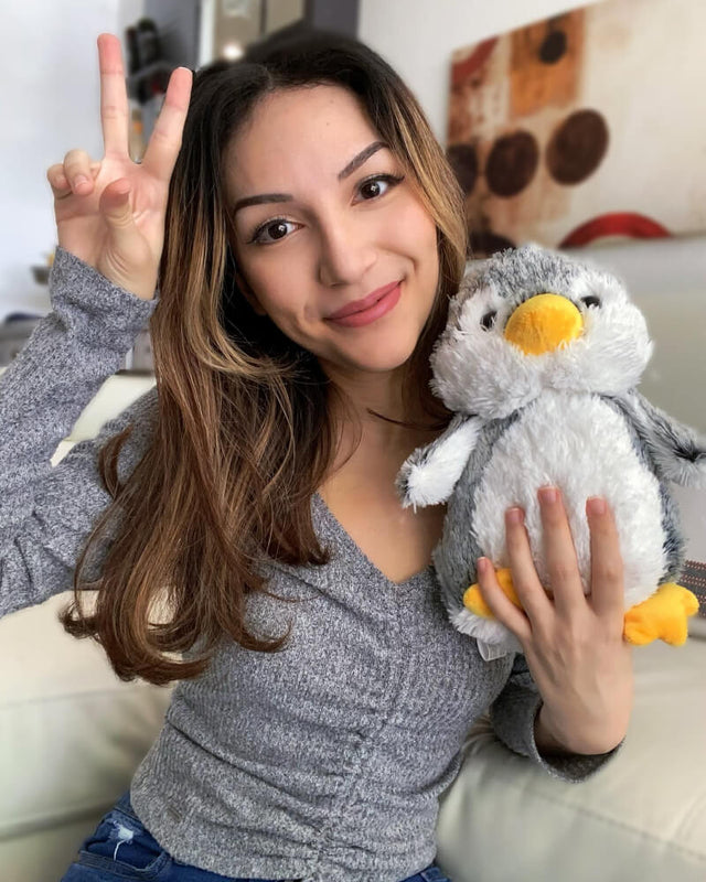 Photo of person making peace sign with hand while smiling and holding grey and white Pepper the Penguin plushie
