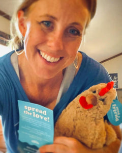 Photo of person smiling while holding tan Rowdy the Rooster plushie and a promotional card
