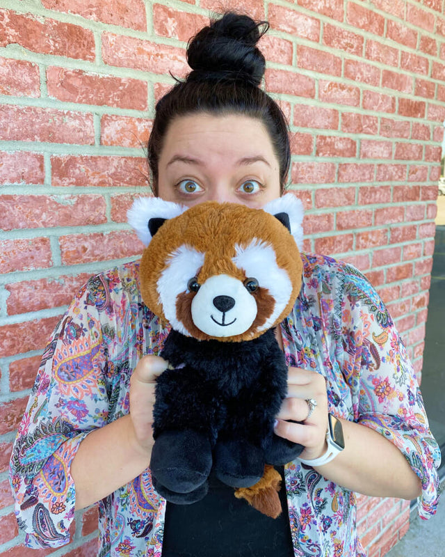 Photo of person holding brown, black, and white Rusty the Red Panda plushie in front of face with surprised eyes
