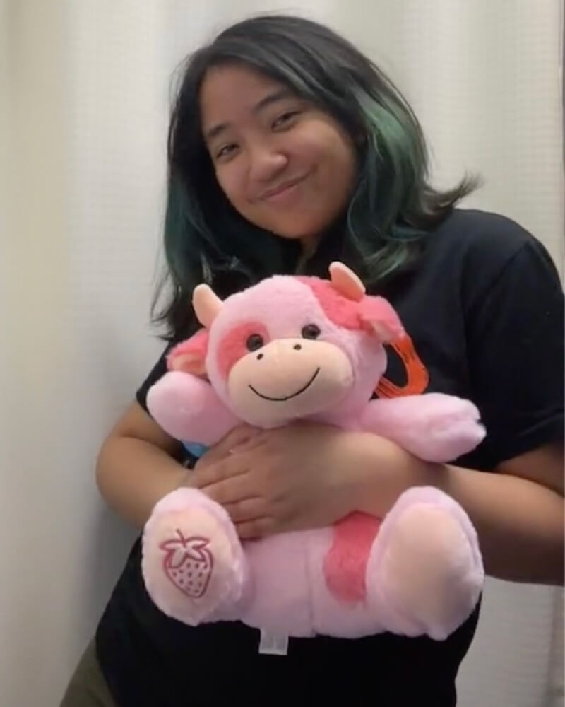 Photo of person smiling while holding Sally the Strawberry Cow plushie